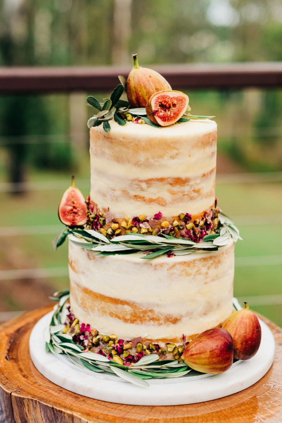 A two-tier naked cake decorated with figs and olive leaves