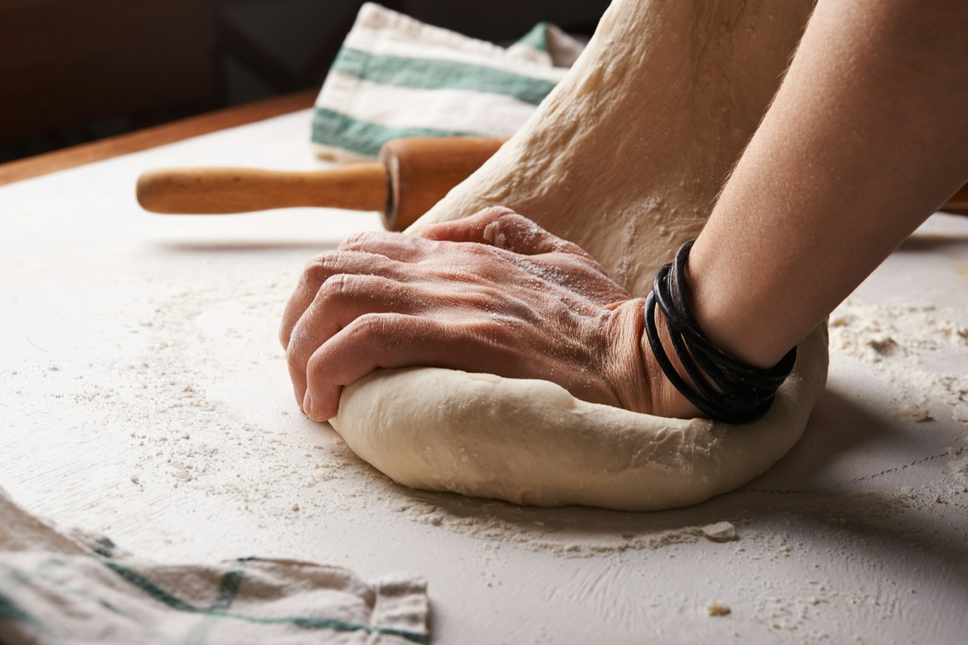 Hands kneading dough on a floured kitchen table